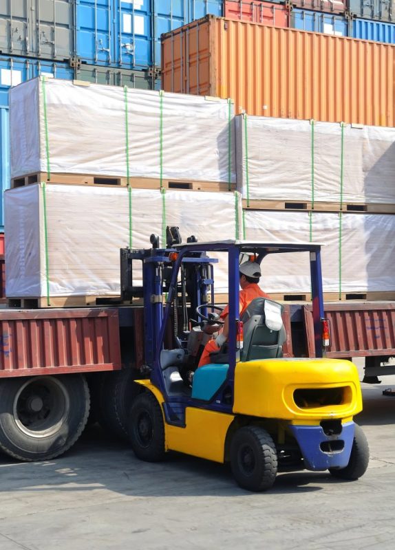 Workers unloading goods from a shipping container using forklifts.
